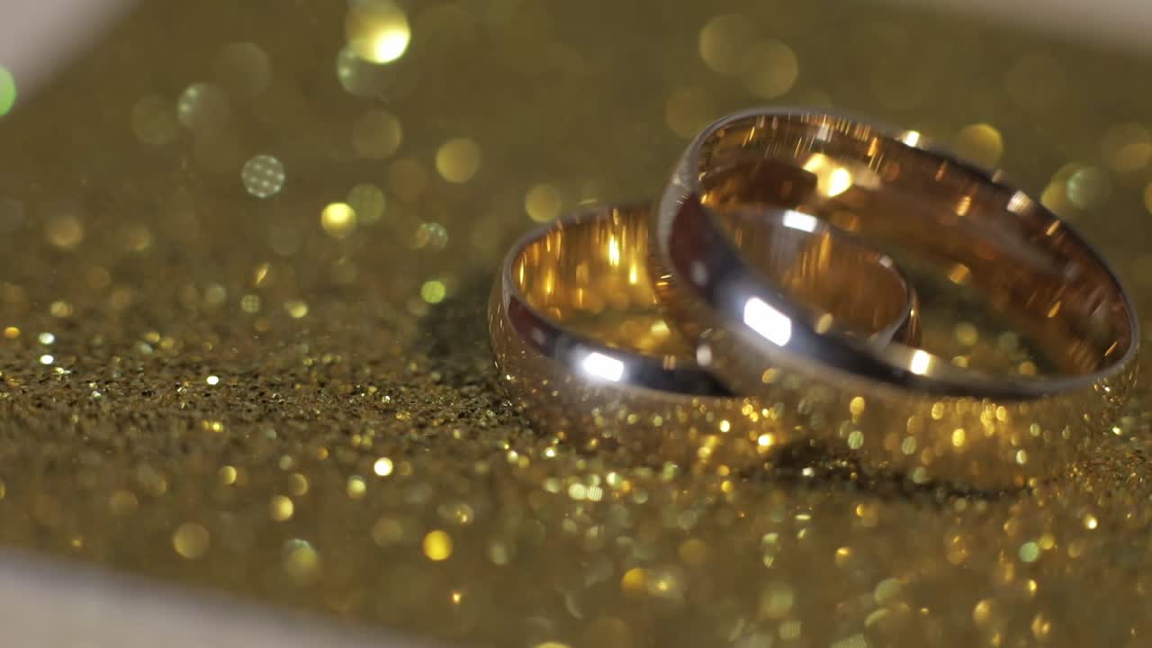 Wedding gols rings lying on shiny glossy surface. Shining with light. Close-up