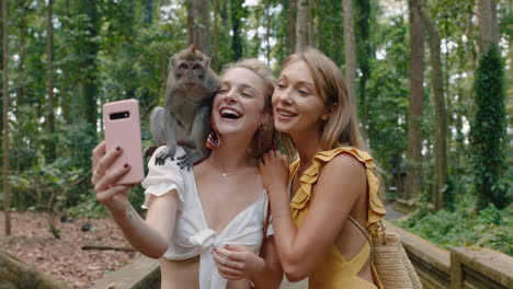 two women using smartphone taking photo of monkey sitting on shoulder girl friends having fun posing with monkeys at wildlife zoo tourists travel bali