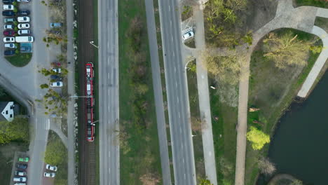 aerial view of a red tram moving along a track parallel to a tree-lined road, with a canal visible to the right