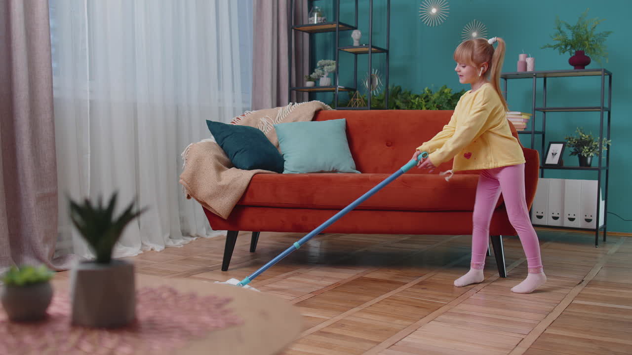 Child girl kid washes floors with a mop in domestic living room dancing, singing in positive mood
