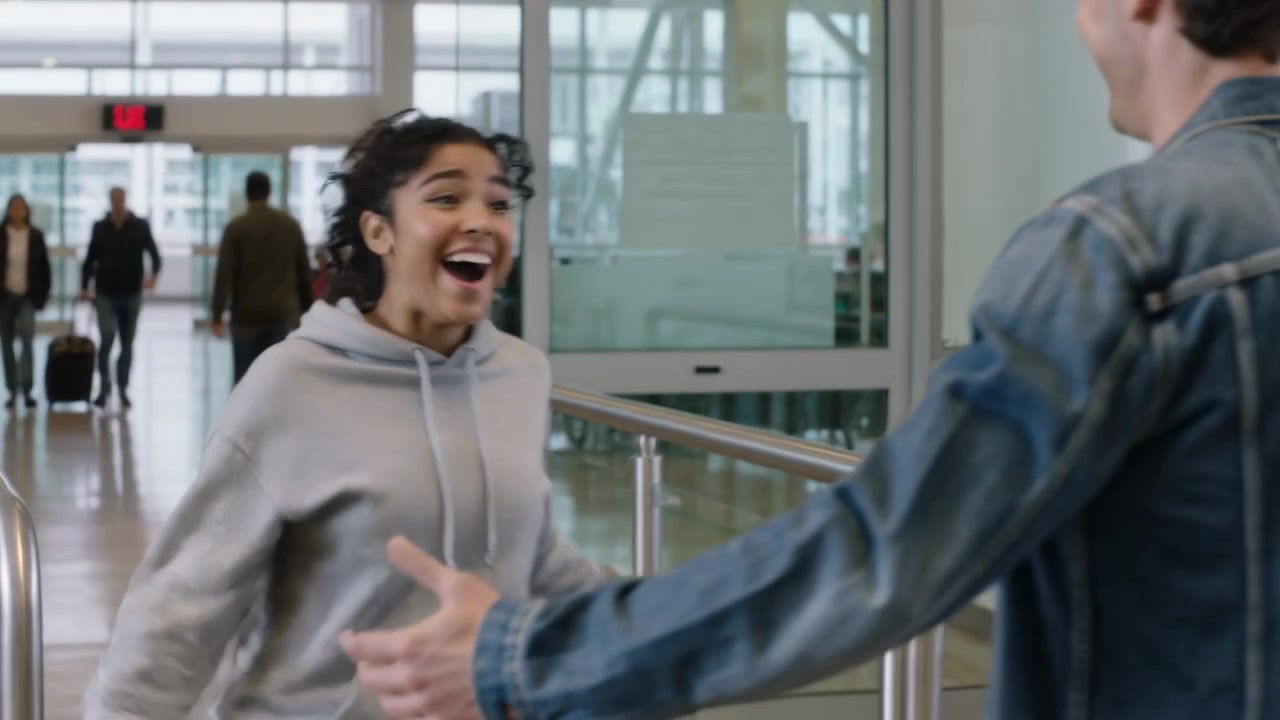 Spotting partner woman in hoodie running pulling rolling suitcase to man hugging reunion at airport