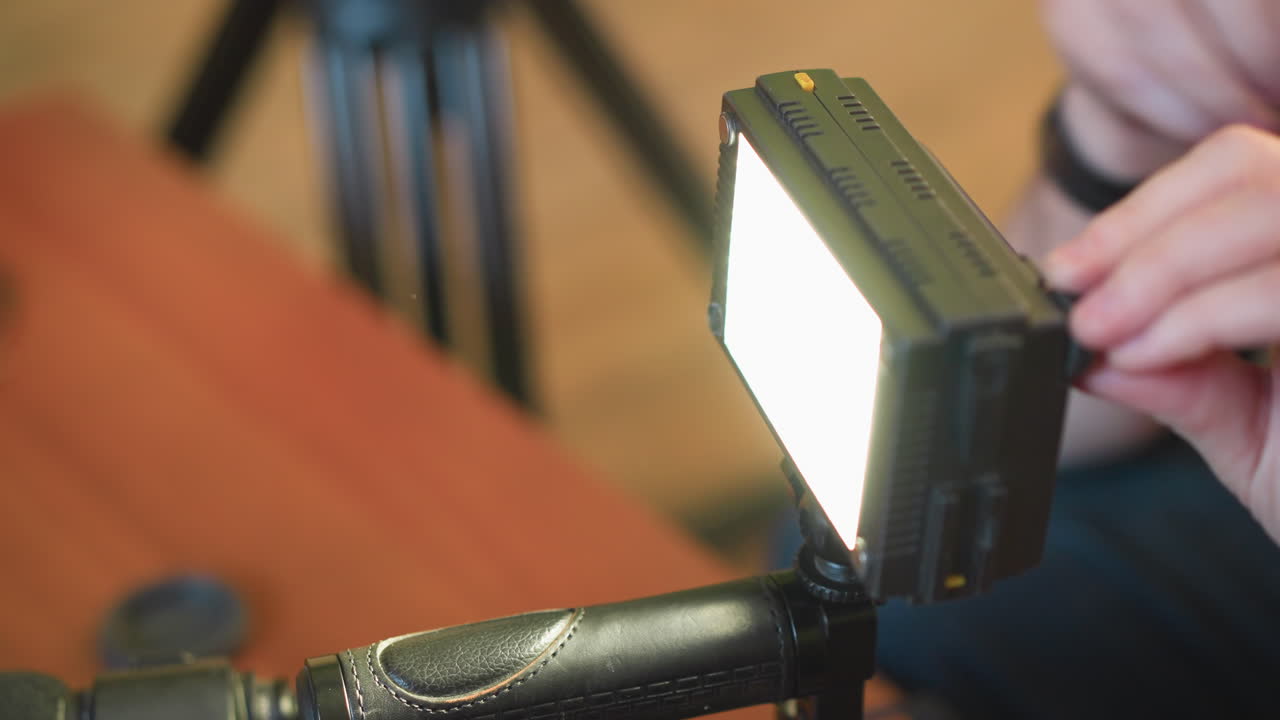 Lighting operator adjusts led light fixture on tripod in studio setting. Focused on proper setup for shoot, ensuring quality lighting for professional filming