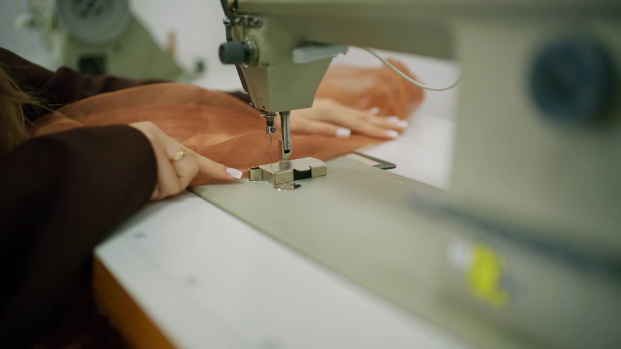 Primer plano de una persona guiando tela transparente marrón bajo la aguja de una máquina de coser industrial