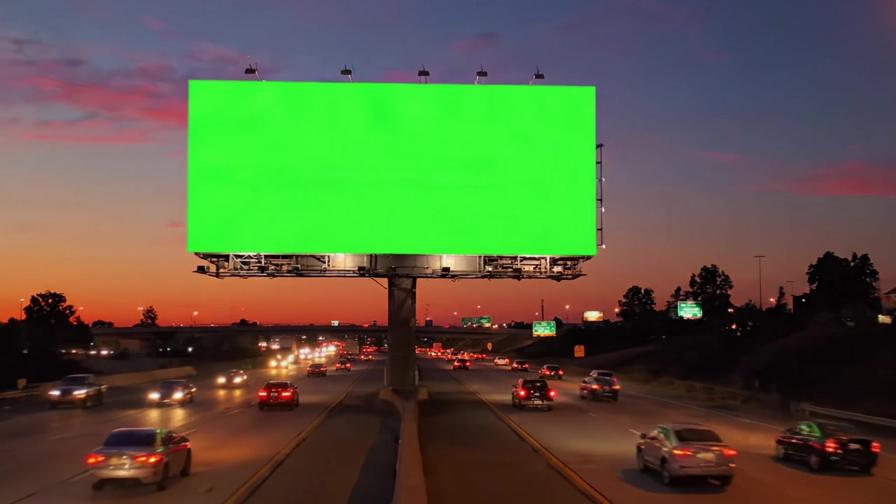 Una Vibrante Valla Publicitaria Verde Ilumina el Cielo Nocturno Sobre una Autopista Concurrida, Donde los Vehículos Navegan el Paisaje Urbano y el Atardecer Transiciona al Crepúsculo
