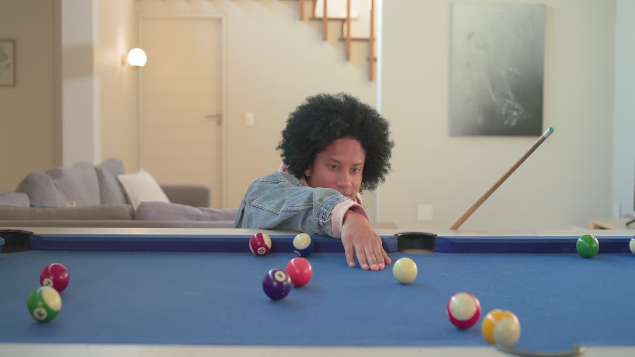 African American man surveying balls and chalking cue on home pool table before striking shot