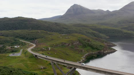 wide revealing drone shot of the kylesku bridge in north-west scotland that crosses the loch a' chàirn bhàin in sutherland, with mountains in the distance