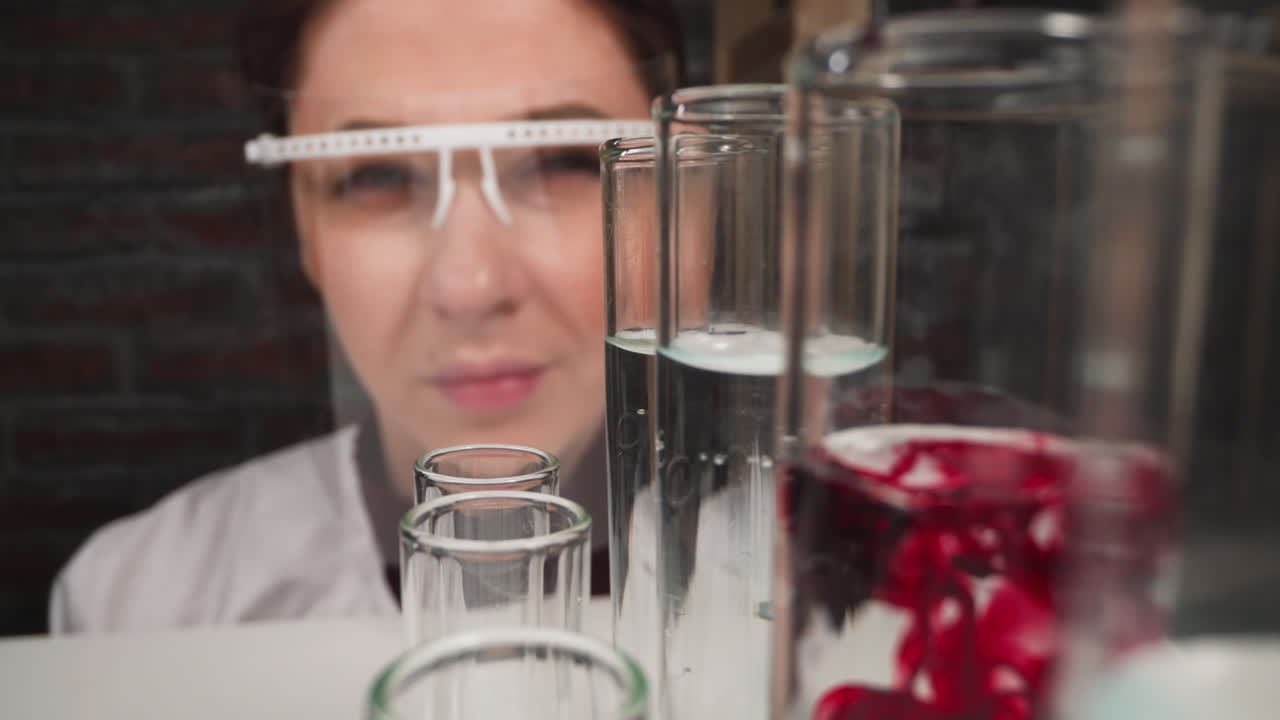 asistente de laboratorio con escudo facial gotea líquido rojo en el tubo