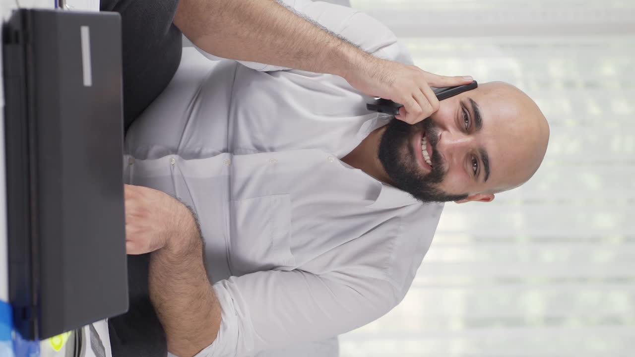 Vertical video of Home office worker man talking on the phone happily.