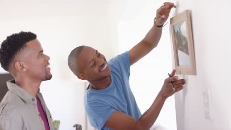 happy african american gay male couple hanging picture on wall and embracing, slow motion