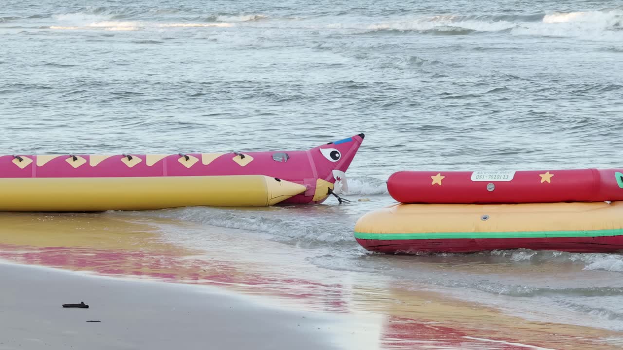Vibrant inflatable boats rest on the sandy beach, with gentle ocean waves in the background.