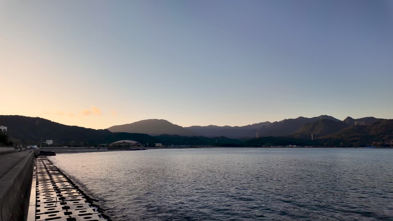 Calm sea reflecting the golden hour light with a mountain range in the background in Nachi Bay. establishing shot
