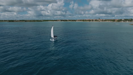 exciting drone shot of a sailing yacht leaving the shoreline and venturing into the vast ocean, revealing a spectacular view of the surrounding beach, green jungle and picturesque holiday apartments