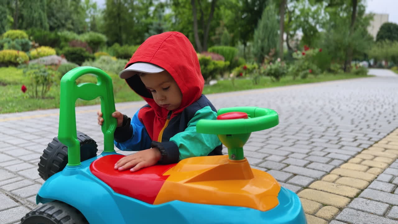 Adorable Caucasian toddler wearing jacket plays with toy car in the park. Baby boy on the walk in autumn.
