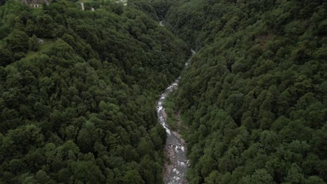 Remote-natural-river-flowing-through-a-forest-valley,-small-church-on-the-hill