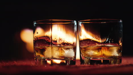 Dos-Vasos-De-Whisky-Se-Colocan-Sobre-La-Mesa-En-El-Fondo,-Un-Fuego-Arde-En-La-Chimenea