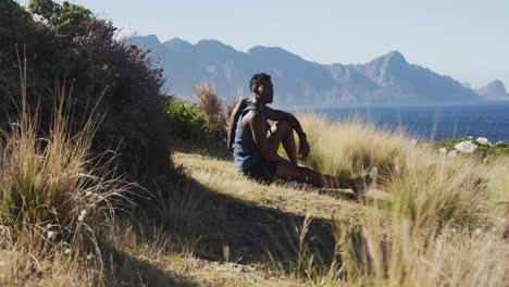 african american man cross country running in by the coast sitting and taking a break