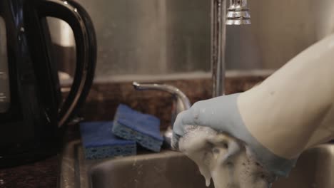 a hand squeezing a dishwashing sponge in the kitchen sink - close up shot