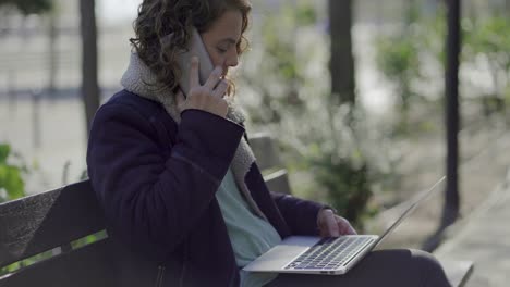 Focused-businesswoman-having-conversation-through-smartphone-and-using-laptop