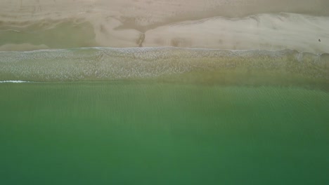 Wellen-Fließen-Ruhig-Entlang-Der-Küste,-Während-Eine-Person-Am-Weißen-Sandstrand-Entlang-Geht