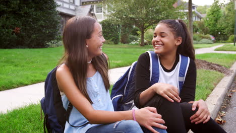 two teen girlfriends sit at the roadside smiling to camera