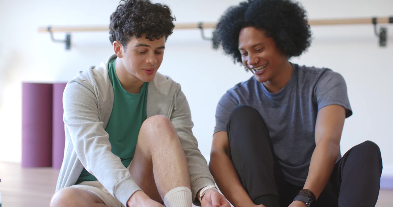 African American male friends sitting in studio tying shoes, phone between them, starting workout