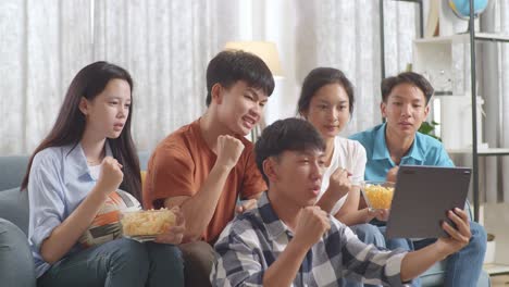 asian teenagers cheering and watching football game on tablet at home