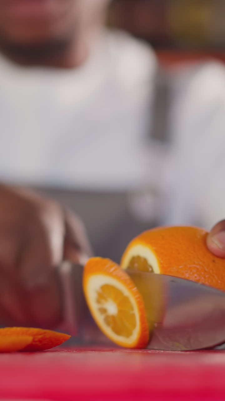 Barman cuts juicy orange on cutting board closeup. African American bartender prepares cocktail with citrus fruit for client. Fresh beverage preparation