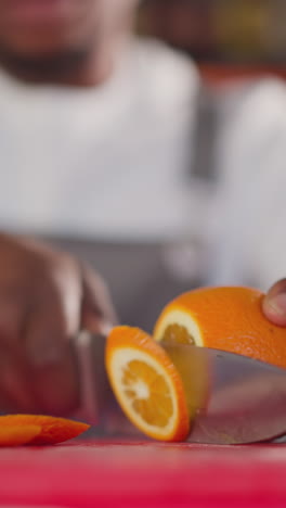 el camarero corta una naranja jugosa en un primer plano de la tabla de corte. el camarero afroamericano prepara un cóctel con cítricos para el cliente. preparación de bebidas frescas
