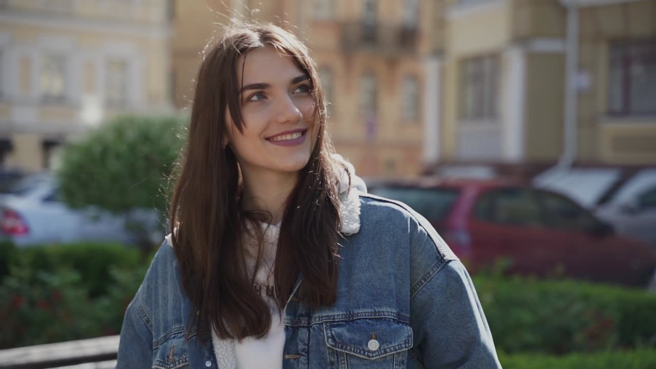 mujer joven y guapa mirando a la cámara y sonriendo mientras alguien habla o la mira al aire libre
