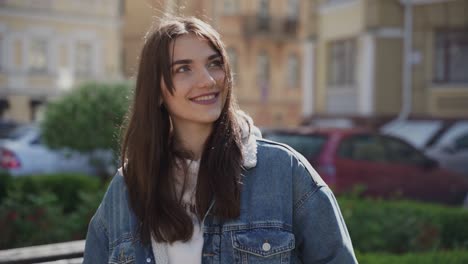 Pretty-Young-Woman-Looking-At-Camera-And-Smiling-While-Someone-Talks-Or-Looks-At-Her-Outdoors