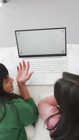 slow-motion vertical video shows joyful biracial mother and daughter using laptop