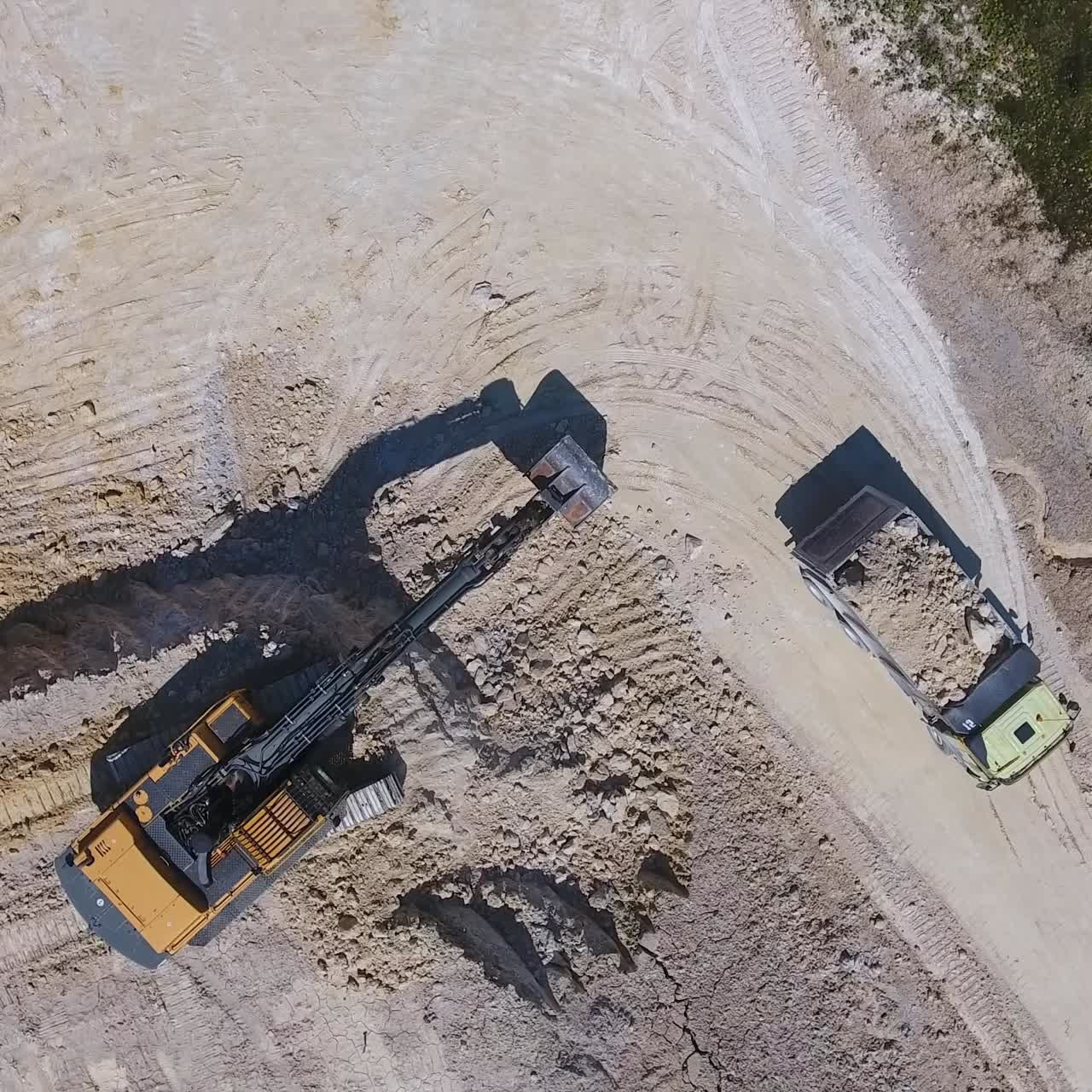 Modern excavator shoveling kaolin clay on the territory of quarry. Loaded truck leaving the site for industrial plant