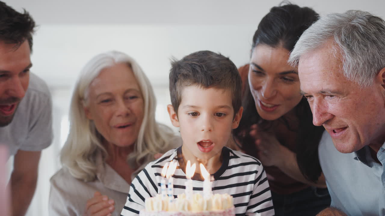 Familie i flere generationer fejrer fødselsdag med barnebarn derhjemme, mens han puster lysene ud