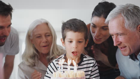 multi generation family celebrating birthday with grandson at home as he blows out candles