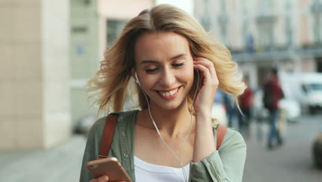 close-up view of caucasian blonde woman walking down the street and listening to music with headphones