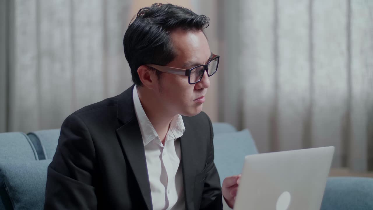 primer plano de un hombre de negocios asiático con chaqueta y pantalones cortos pensando y luego levantando el dedo índice mientras trabaja con una computadora portátil en casa