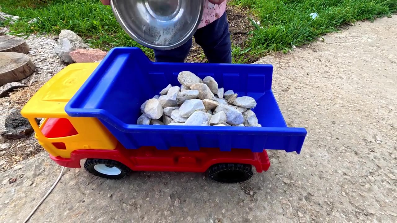 Un bambino piccolo esplora all'aperto, giocando felicemente con un camion giocattolo e delle rocce. La vista ravvicinata mostra il divertimento dell'infanzia e il gioco immaginativo