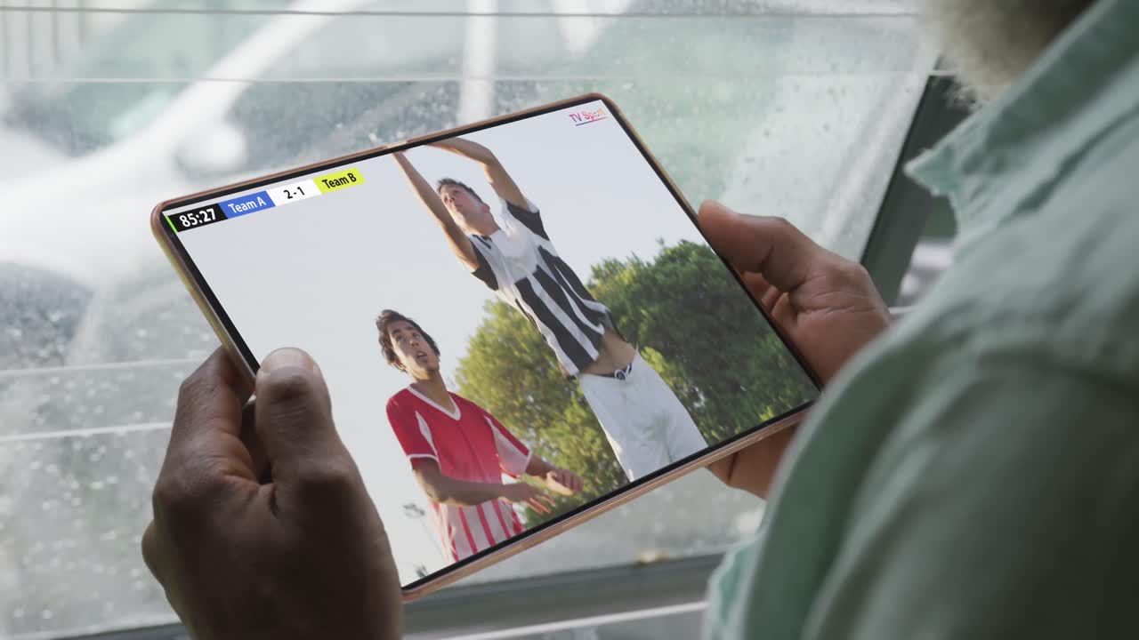 video de un hombre afroamericano sentado en el sofá y viendo fútbol en la tableta en casa