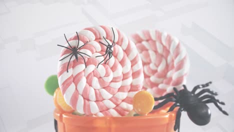 Spiders-falling-over-in-halloween-pumpkin-bucket-filled-with-candies-against-3d-concentric-shapes