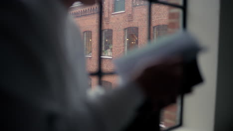 silhouette reading a book by a window with a brick building view