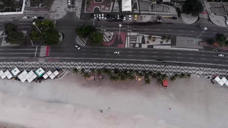 Aerial-backwards-movement-tilting-up-revealing-a-calm-and-empty-Copacabana-beach-and-boulevard-with-waves-rolling-in-at-first-light-early-morning-sunrise