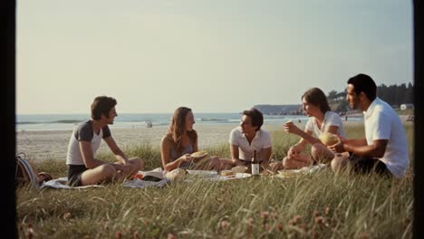 a joyful gathering of friends enjoying a beach picnic, sharing laughter and food on a sunny day by the ocean, framed by the beauty of the sandy shore and grassy landscape