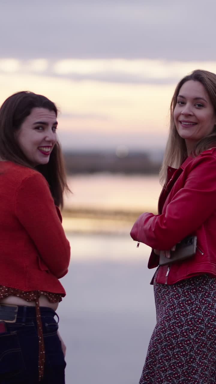 Twee vrouwen in het rood staand vlak bij een rivier bij zonsondergang