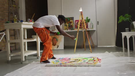 artista masculino afroamericano vertiendo pintura con un pincel de pintura en el lienzo en un estudio de arte