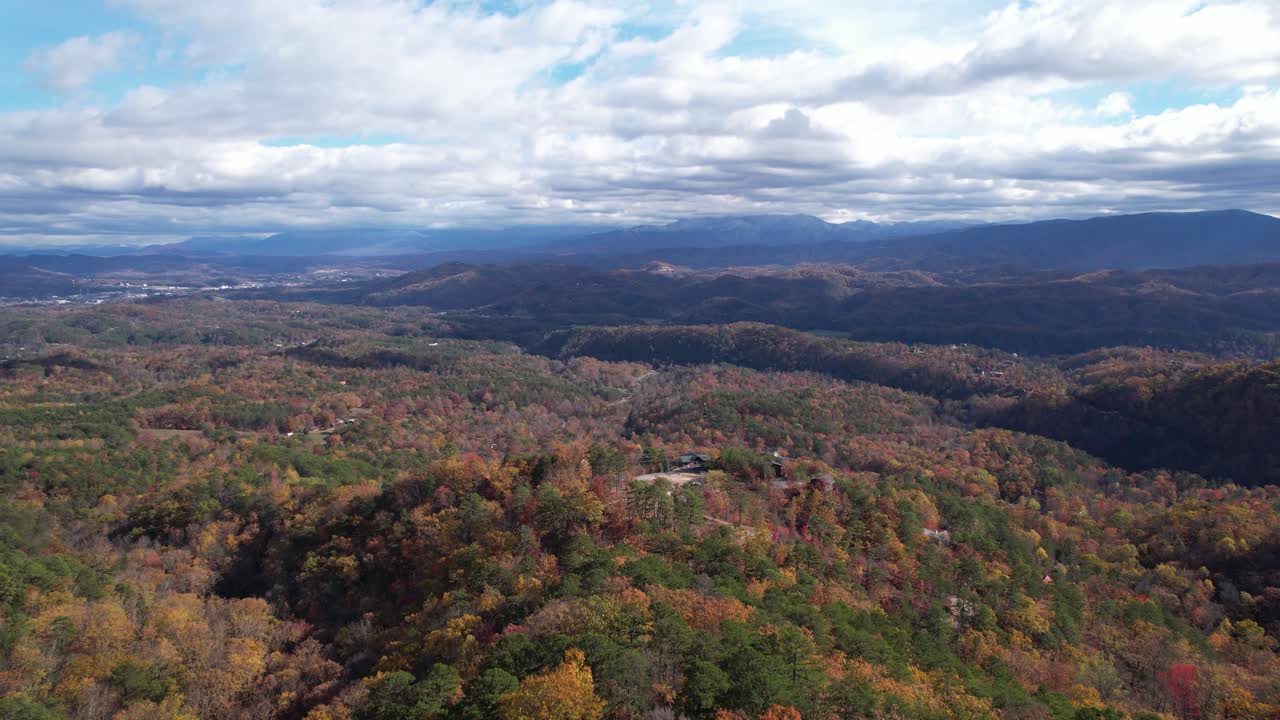 Drone ascending and then zooming in to reveal mountain cabins surrounded by lush forest and expansive mountainous terrain.