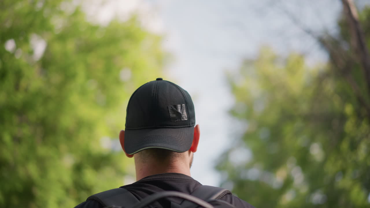 Man With Bag Observes Sky, Person Carrying Pack Gazes Upward At Branches And Blue Sky, Male Figure With Backpack Meanders Slowly Through Springtime Greenery Observing Clouds And Tree Limbs