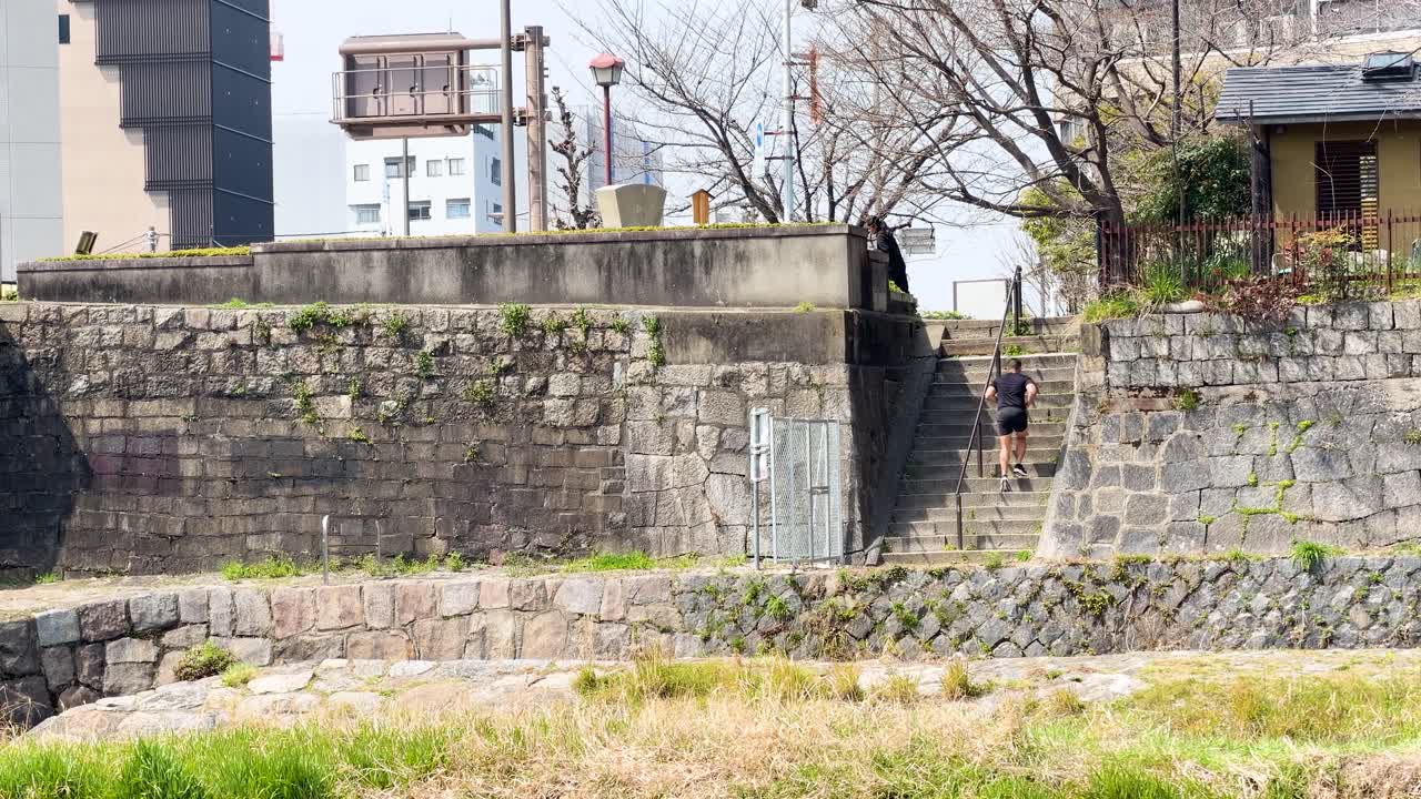 Un uomo giapponese in forma sale di corsa delle scale di pietra contro un muro alla luce del giorno.