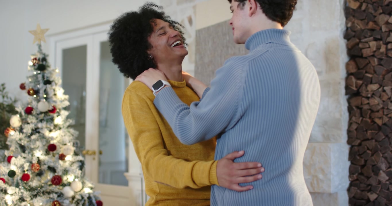 African American men in mustard blue sweaters holding shoulders after joke smiling at home by tree