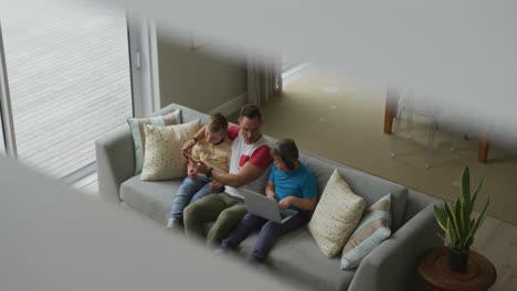 caucasian father with two sons sitting in living room and using laptop