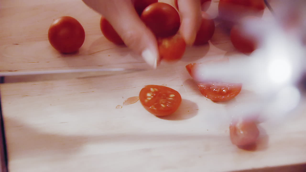 Woman cutting cherry tomatos. Close up of a female cutting tomatos in the kitchen on a wooden plate.